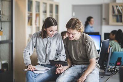 High school students sharing digital tablet while sitting on desk in computer lab