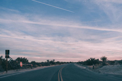 Road by trees against sky during sunset