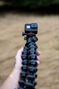 Hand holding tripod with action camera over brown grass in field