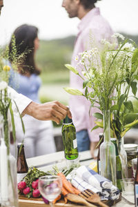 Cropped image of man holding beer bottle over dining table during dinner party in backyard