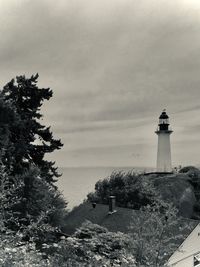 Lighthouse amidst buildings and sea against sky