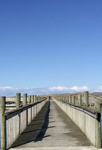View of wooden bridge against clear blue sky
