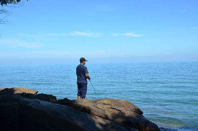 Man fishing in sea against sky