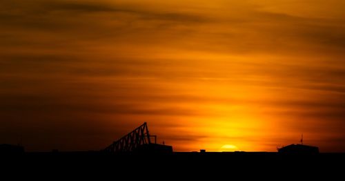 Silhouette bridge over buildings against dramatic sky during sunset