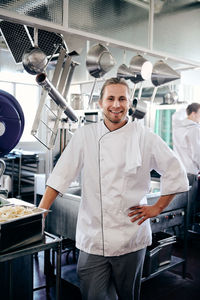 Portrait of smiling male chef standing with hand on hip in kitchen