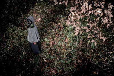 High angle view of person wearing gas mask while standing on grassy field in forest