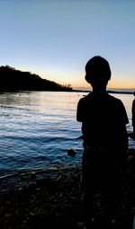 Silhouette boy standing at beach against clear sky