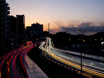 Light trails on road amidst buildings against sky at night