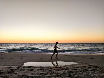 Silhouette man running on beach against clear sky