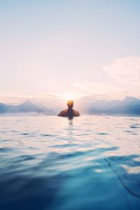 Man swimming in sea against sky during sunset