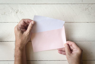 Directly above shot of cropped hands holding envelope at table