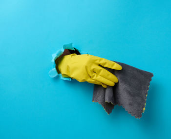 Hand in a yellow rubber cleaning glove holds a dry rag on a blue background. part of the 