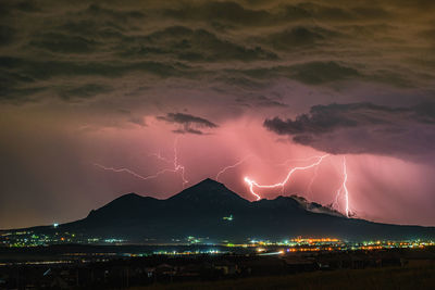 Lightning over illuminated cityscape against sky at night