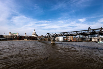 Bridge over river by buildings against sky in city