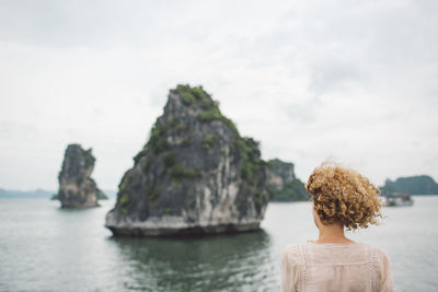 Rear view of woman standing on rock by sea against sky