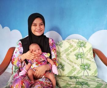 Portrait of mother sitting with baby girl in lap at home