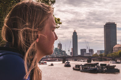 Profile view of young woman against river in city