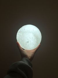Cropped hand of person holding crystal ball against wall
