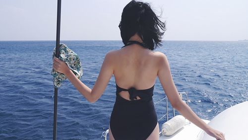 Rear view of young woman standing in sea against clear sky