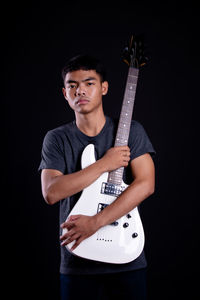 Portrait of a young man playing guitar against black background