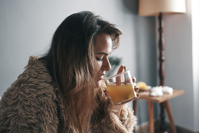 Close-up of woman drinking lemon tea sitting on bed