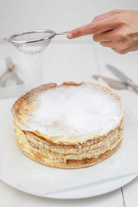 Cropped hand sprinkling powdered sugar on dessert