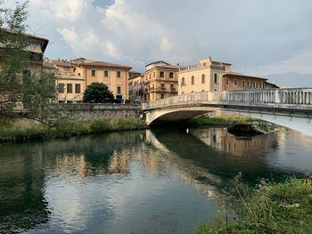 Arch bridge over river by buildings against sky