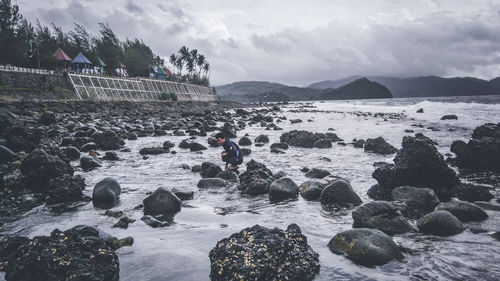 Side view of man crouching on rocks at beach