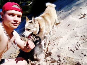 Portrait of shirtless man kneeling by dog at sandy beach