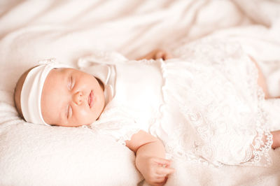 Sleeping cute baby infant girl wear stylish white dress and headband in bed.