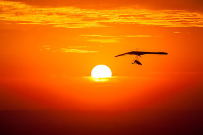 Silhouette bird flying against orange sky