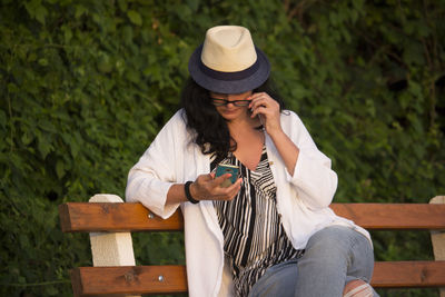 Young woman using phone while sitting on bench