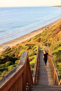 Rear view full length of woman standing on wooden steps at beach