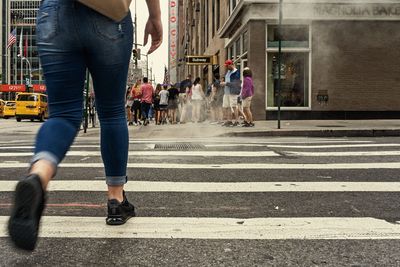 Low section of woman walking on road in city