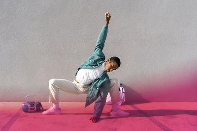 Young man stretching while crouching by radio on footpath