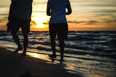 Low section of people walking on shore at beach