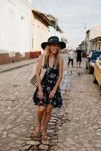 Young woman wearing hat while standing on city street against sky