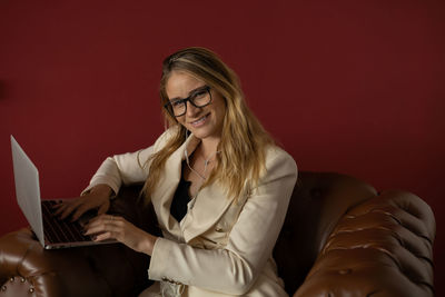 Woman working at home with laptop classic brown arm chair. red  wall home office. gray notebook 