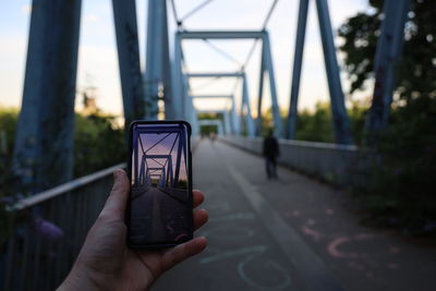 Person holding mobile phone and taking a picture of a bridge 