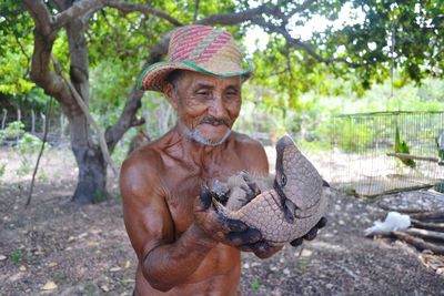 Man holding armadillo while standing against tree