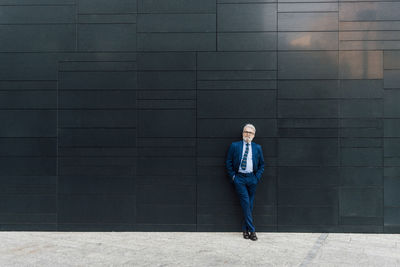 Businessman with legs crossed at ankle standing in front of wall