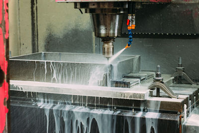 Foamy cutting fluids spraying on spinning metalworking equipment in light modern industrial workshop