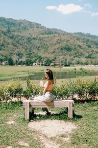 Woman sitting on bench against plants