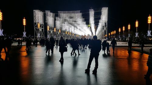 People on illuminated street against sky at night