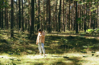 Full length of man standing by tree trunk in forest