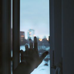 Close-up of hand reaching towards window at home