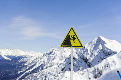 Information sign on snowcapped mountain against sky