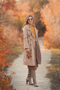 Full length of smiling young woman standing during autumn