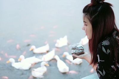 Close-up of young woman feeding duck swimming in lake