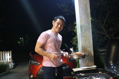 Young man smiling while standing on barbecue at night